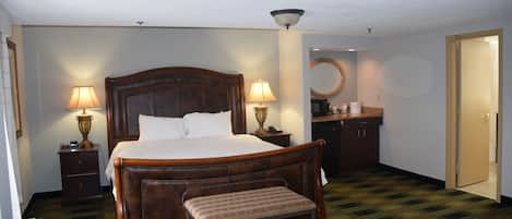 A hotel room with a large bed, bedside lamps, a bench, a mirror, a desk, and a door.