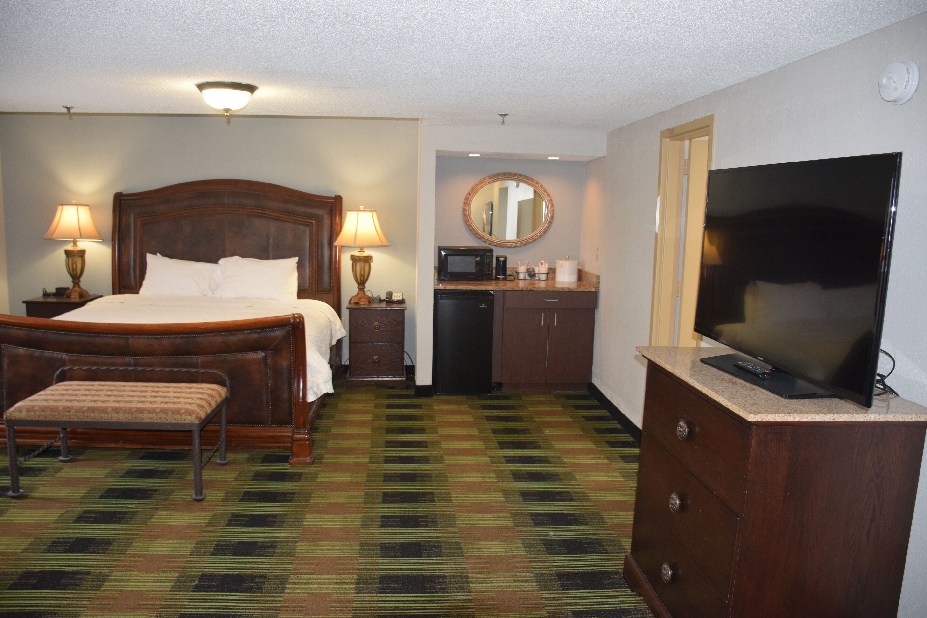 A hotel room with a bed, a bench, a TV, a microwave, a coffee maker, and a mirror.