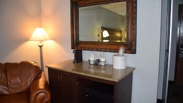 Una habitación de hotel con un sofá de cuero marrón, una máquina de café, un cesto de basura, un dispensador de pañuelos de papel y un espejo en la pared.