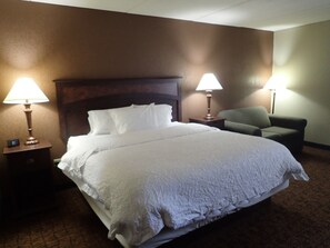 A hotel room with a large bed, two bedside tables with lamps, a green armchair, and a headboard. - Wingate by Wyndham Baltimore BWI Airport (Linthicum Heights)