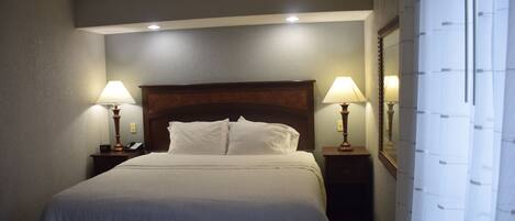A hotel room with a large bed, two bedside lamps, a wooden headboard, and a mirror on the wall.
