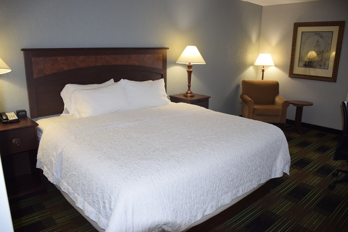 A hotel room with a large bed, two bedside tables, a chair, and a small table.