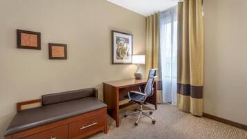 A hotel room with a wooden desk, a black office chair, a brown sofa, and two framed pictures on the wall.
