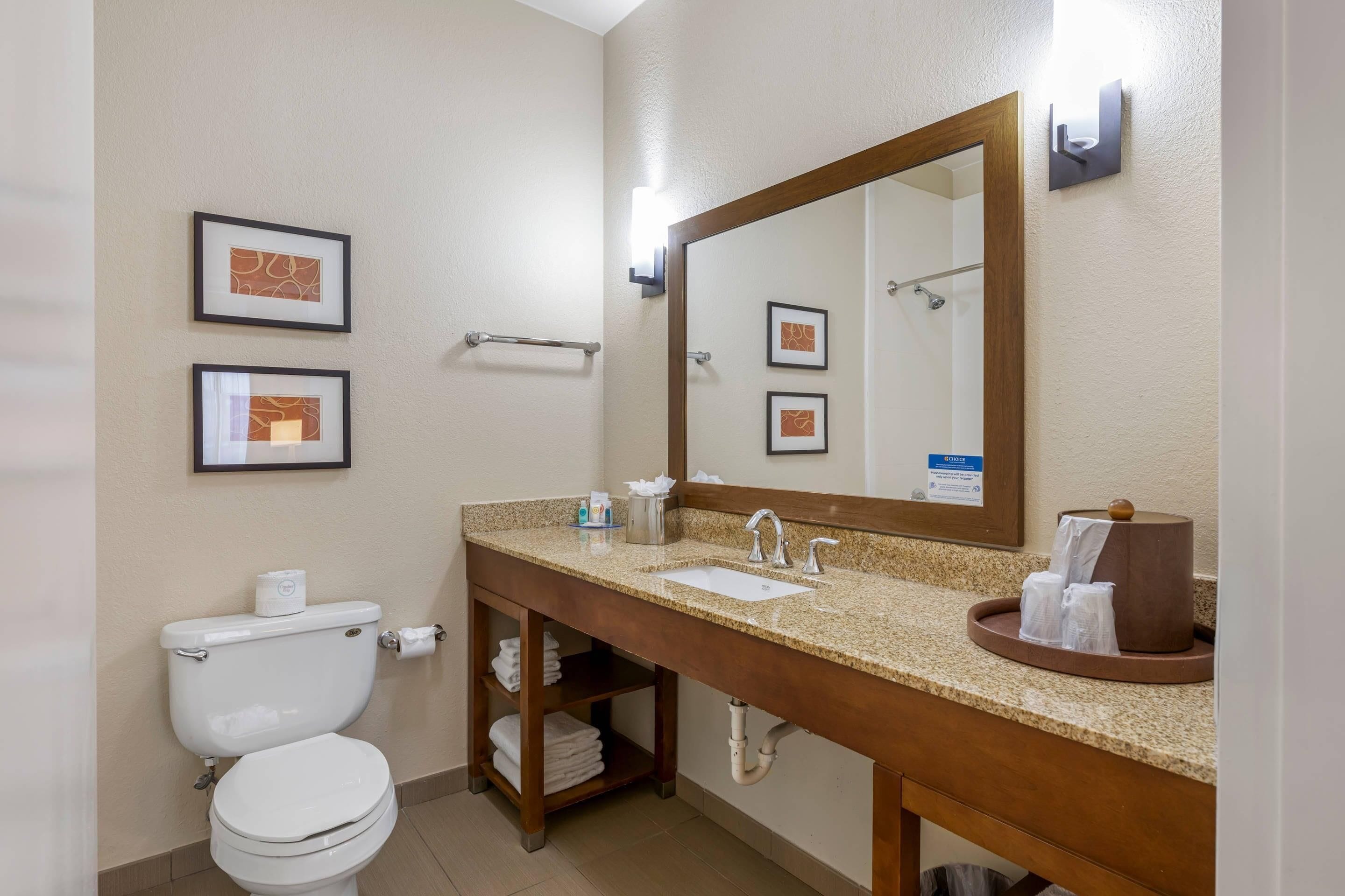 A bathroom with a toilet, sink, and mirror. There are framed pictures on the wall and a towel rack.