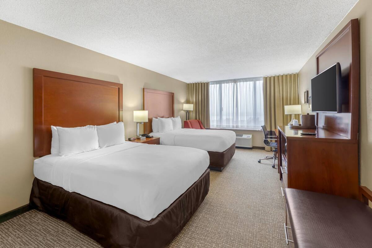 A hotel room with two beds, a desk, a TV, and a window with curtains.