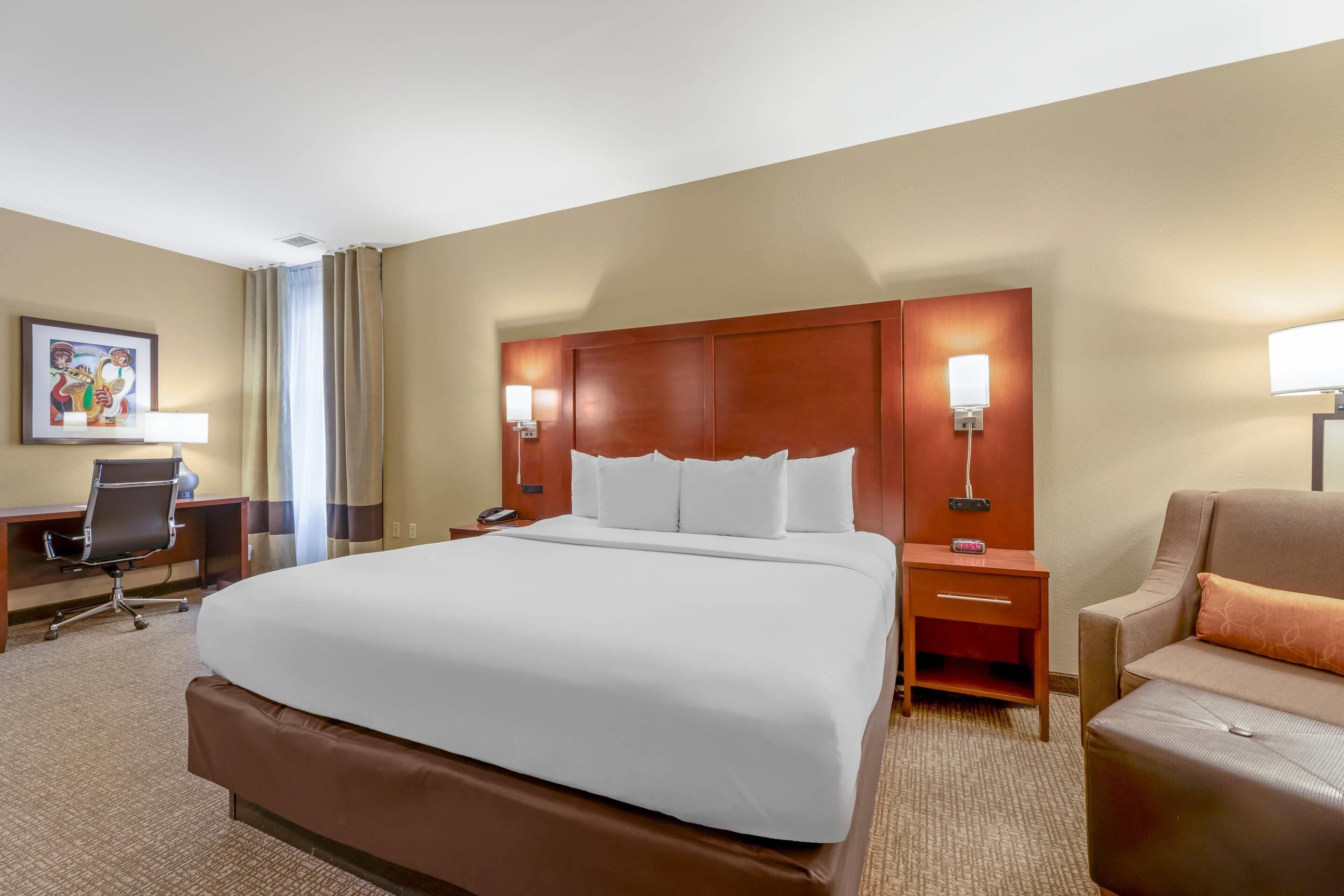 A hotel room with a large bed, a desk, a chair, and a nightstand with lamps.