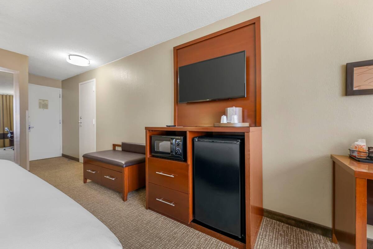 A hotel room with a bed, a small kitchenette with a microwave, refrigerator, and a television mounted on the wall.