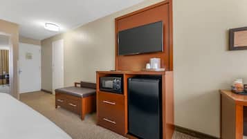 A hotel room with a bed, a small kitchenette with a microwave, refrigerator, and a television mounted on the wall.