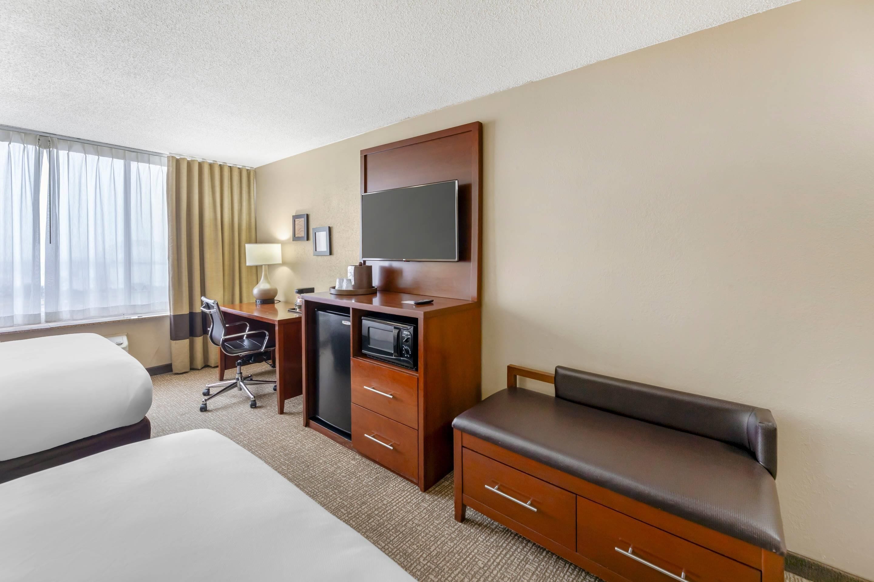 A hotel room with a bed, a desk with a computer, a TV, and a seating area.