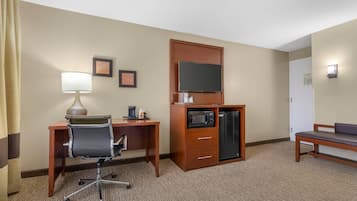 Une chambre d’hôtel équipée d’un bureau, d’une chaise, d’un four à micro-ondes, d’un réfrigérateur et d’un téléviseur posé sur une commode en bois.