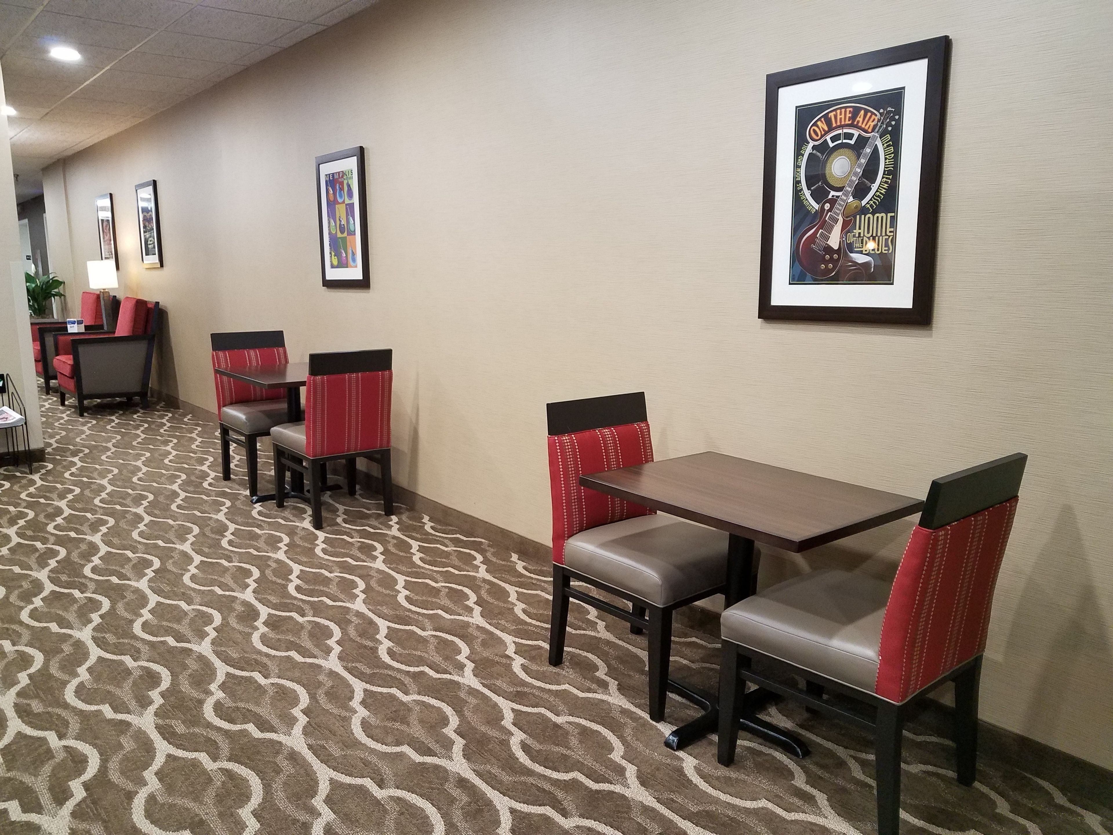 A hotel lobby with a patterned carpet, red and black upholstered chairs, and framed posters on the wall.