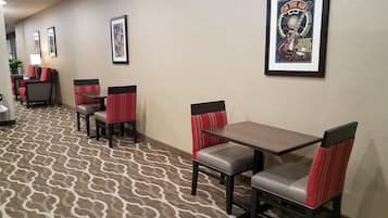 A hotel lobby with a patterned carpet, red and black upholstered chairs, and framed posters on the wall.