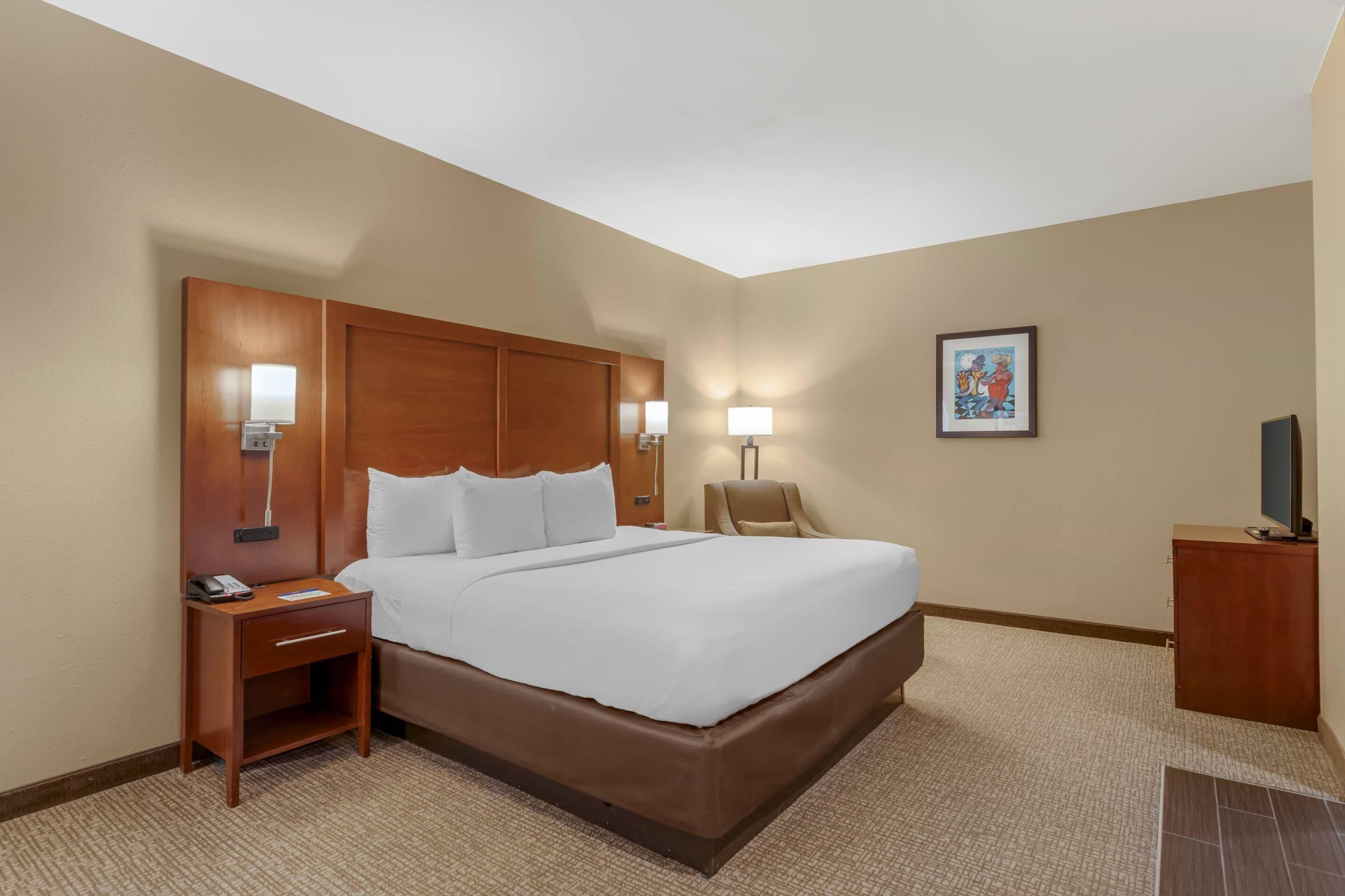A hotel room with a large bed, bedside lamps, a nightstand, a television, and a framed picture on the wall.