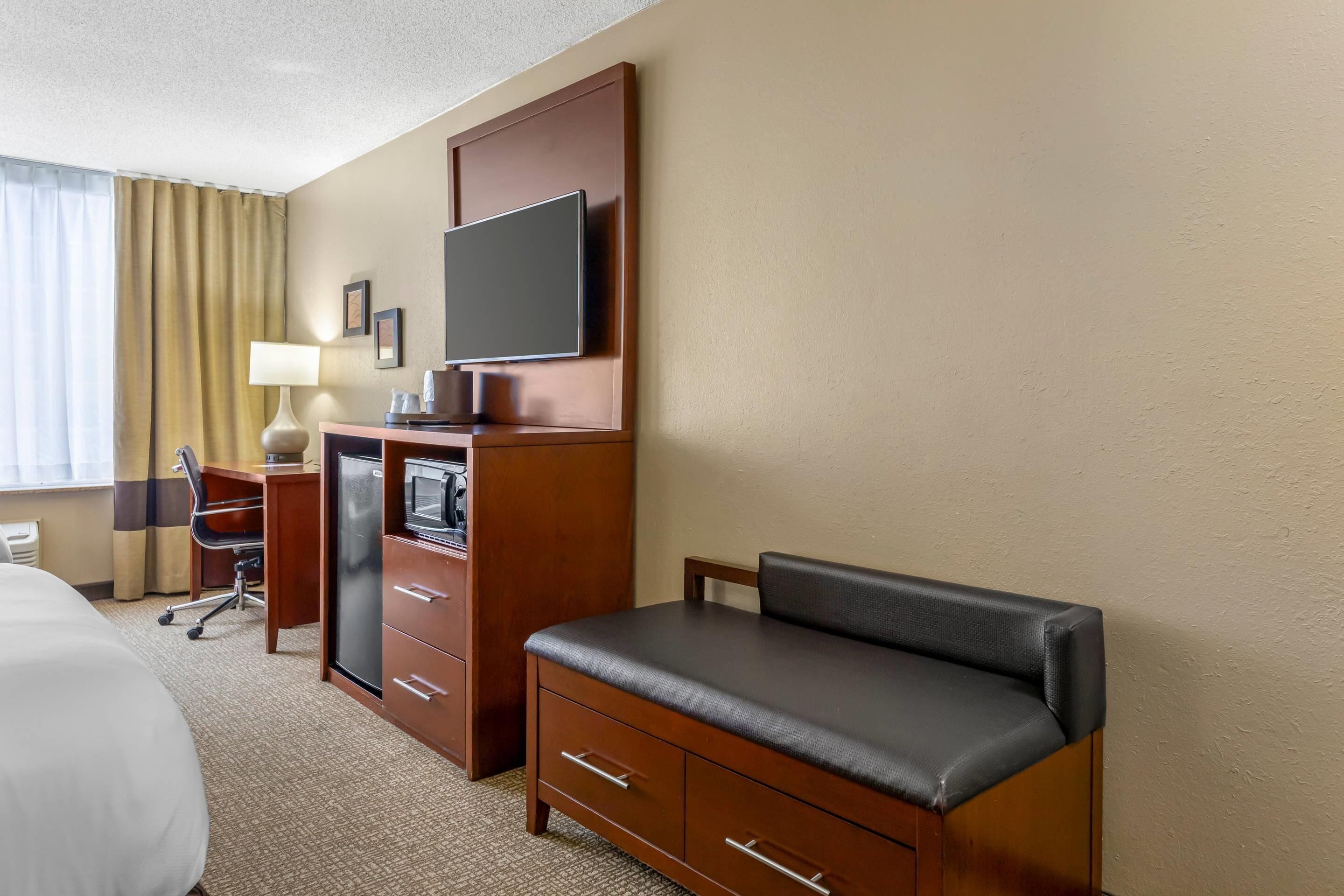 A hotel room with a bed, a desk with a computer, a TV, and a seating area.
