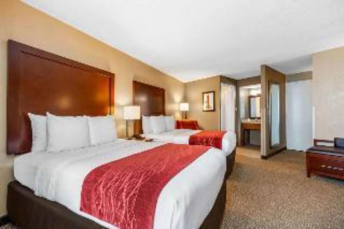 A hotel room with two beds, a wooden headboard, a nightstand, a desk, and a mirror.