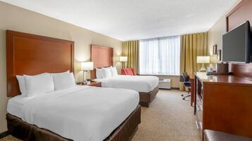 A hotel room with two beds, a desk, a television, and a window with curtains.