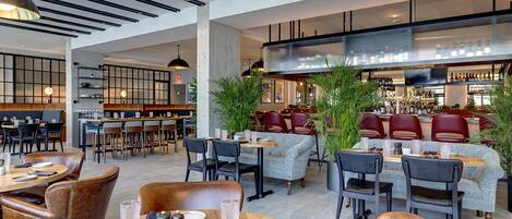 A modern restaurant with high ceilings, exposed beams, and a mix of seating areas including tables and booths.