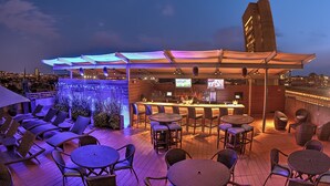 A rooftop bar with outdoor seating, a bar area, and a city view at dusk. - The Colonnade Hotel Back Bay (Boston)