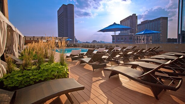 A rooftop pool area with lounge chairs and umbrellas, overlooking a cityscape. - The Colonnade Hotel Back Bay (Boston)