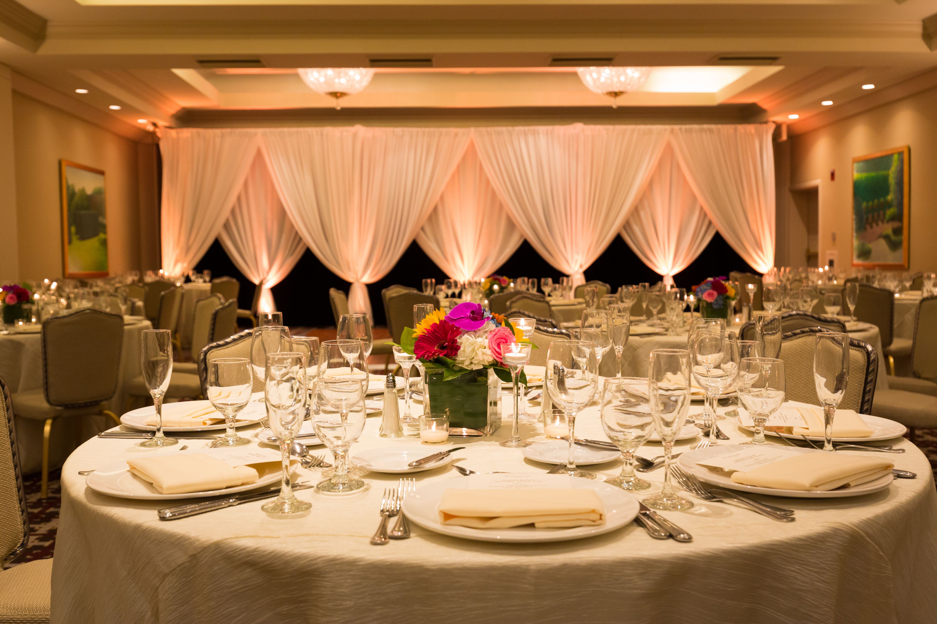A banquet hall with round tables set for dining, featuring white tablecloths, glassware, and floral centerpieces.