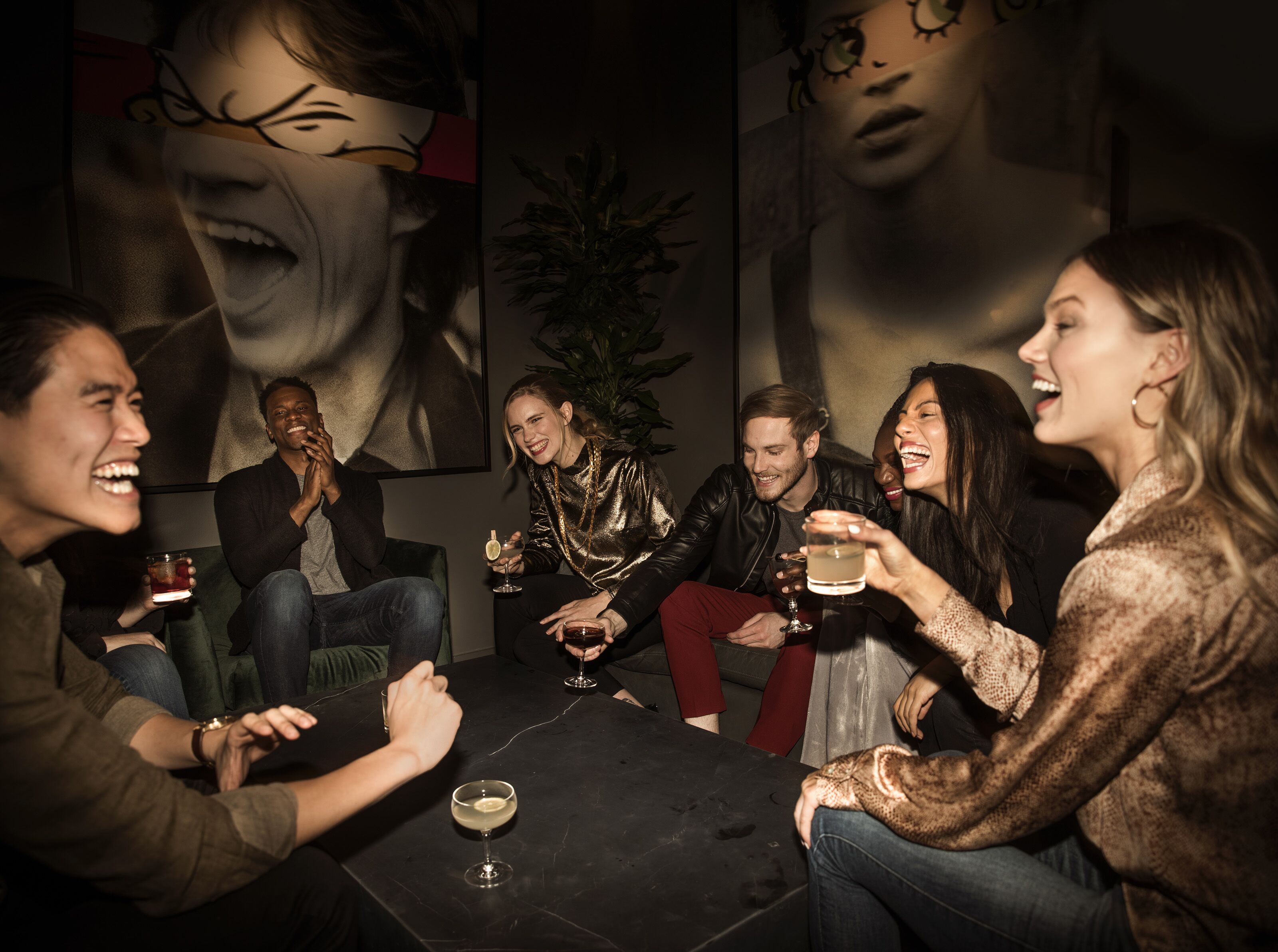 A group of people sitting around a table in a dimly lit room with a large abstract painting on the wall.