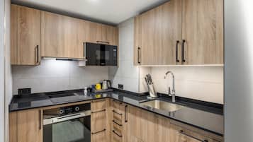 Una cocina moderna con armarios de madera, encimera negra, electrodomésticos de acero inoxidable y horno empotrado.