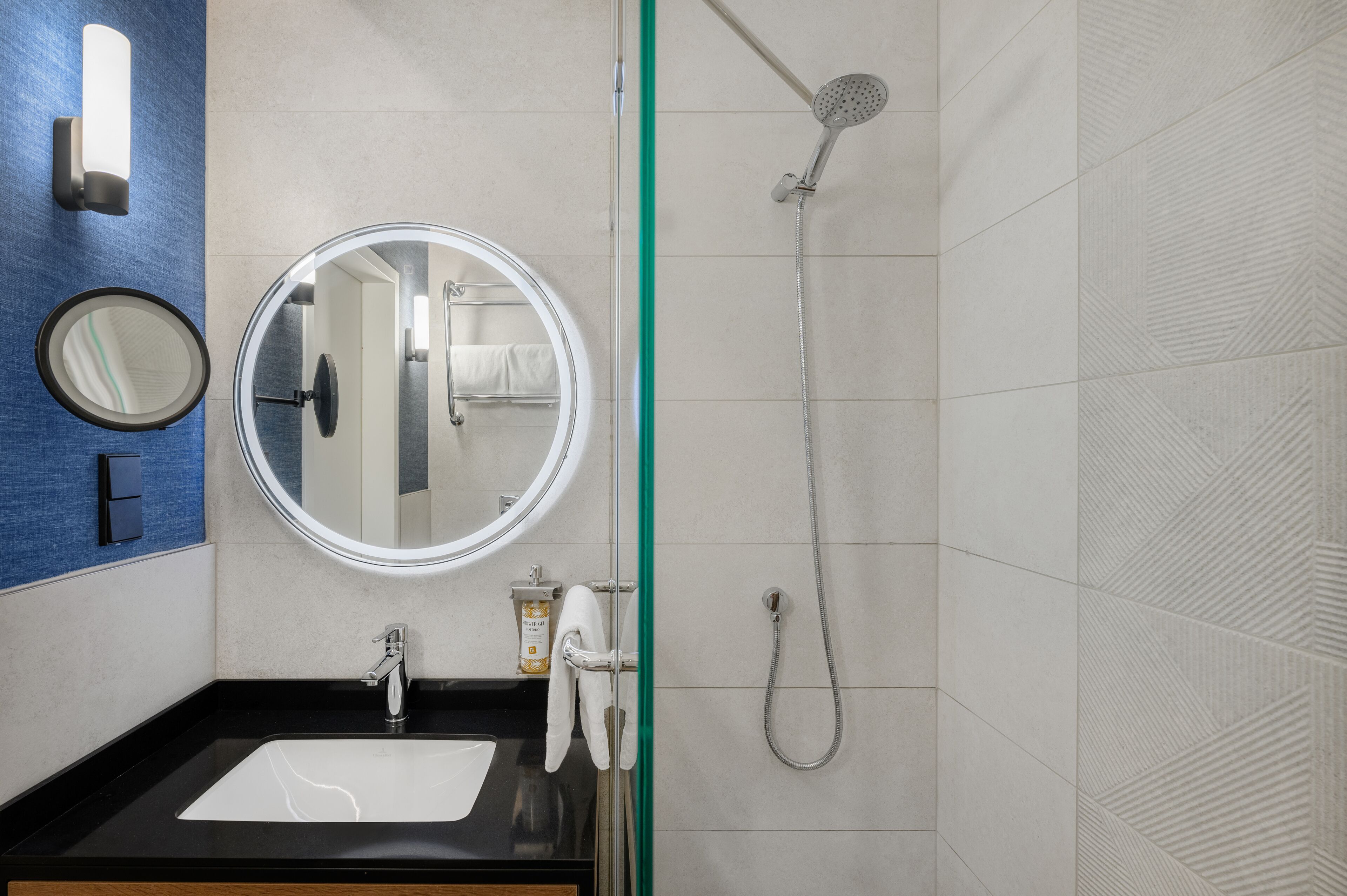Un baño moderno con un lavamanos negro, un espejo redondo, un cabezal de ducha de mano y un perchero.