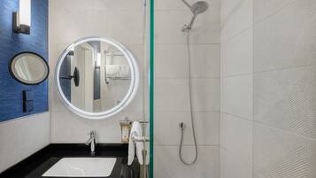 Un baño moderno con un lavamanos negro, un espejo redondo, un cabezal de ducha de mano y un perchero.