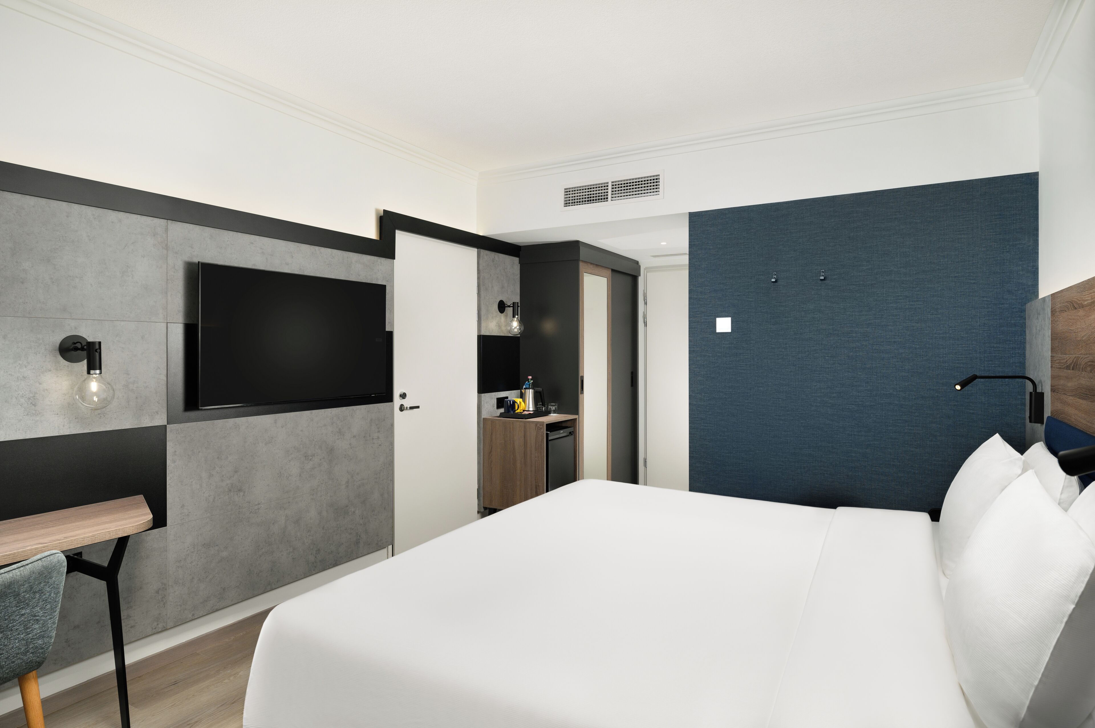 Habitación de hotel moderna con una cama grande, televisión de pantalla plana, escritorio con silla y kitchenette.