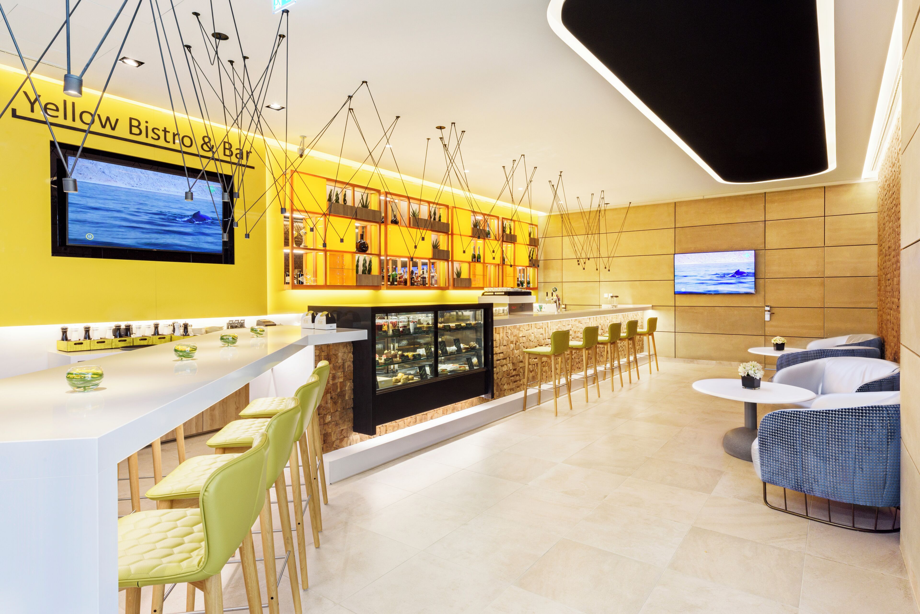 A modern bistro with a yellow and white color scheme, featuring a bar area, seating, and a television screen.