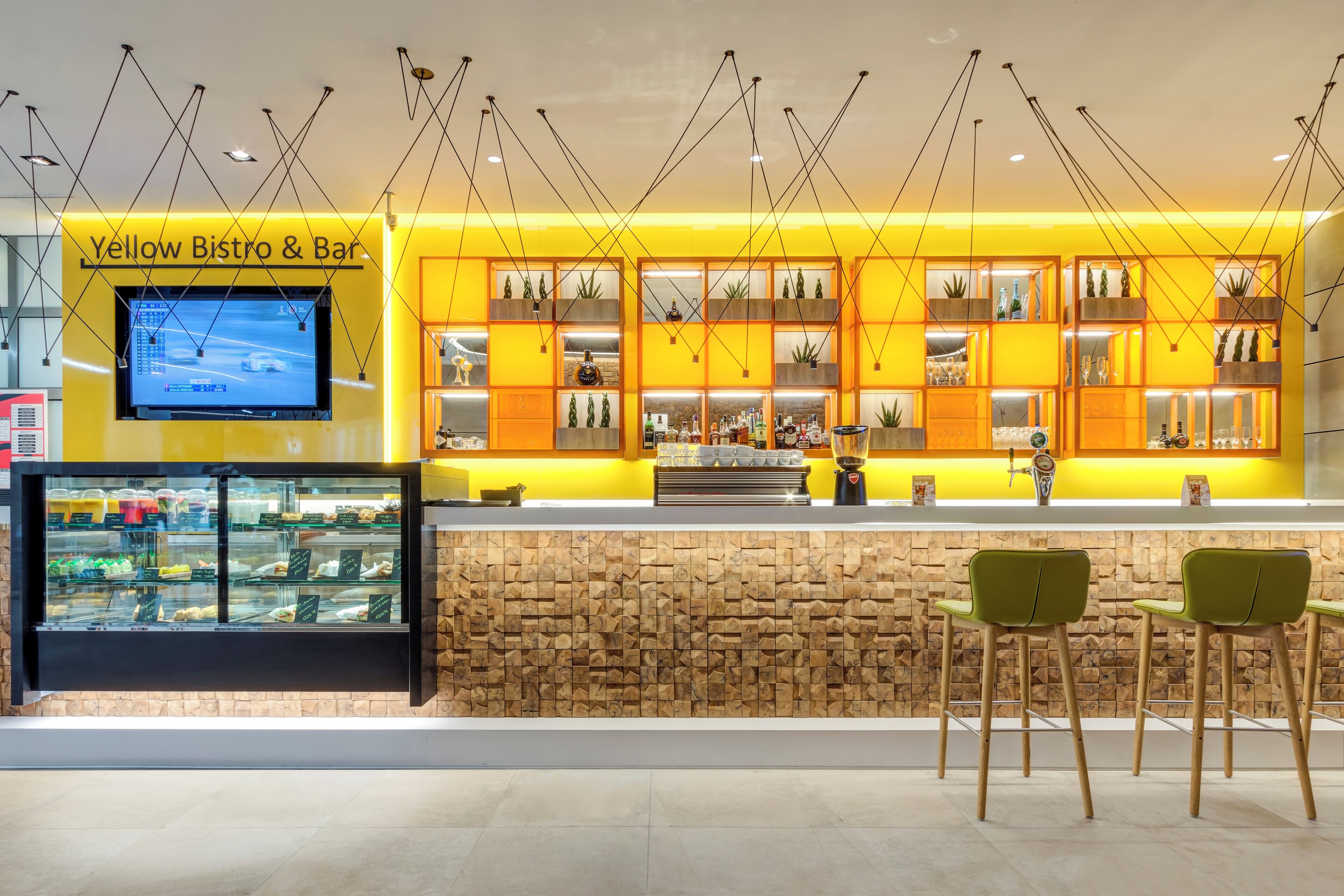 Um Bistro & Bar amarelo com design moderno, apresentando uma parede de pedra, vitrines de vidro e cadeiras verdes.