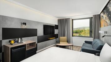 Habitación de hotel moderna con cama, escritorio con cafetera, silla, televisión y vista al exterior.