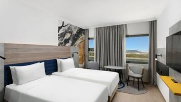 Habitación de hotel con dos camas, una mesita, una silla, televisor y ventana con vistas.