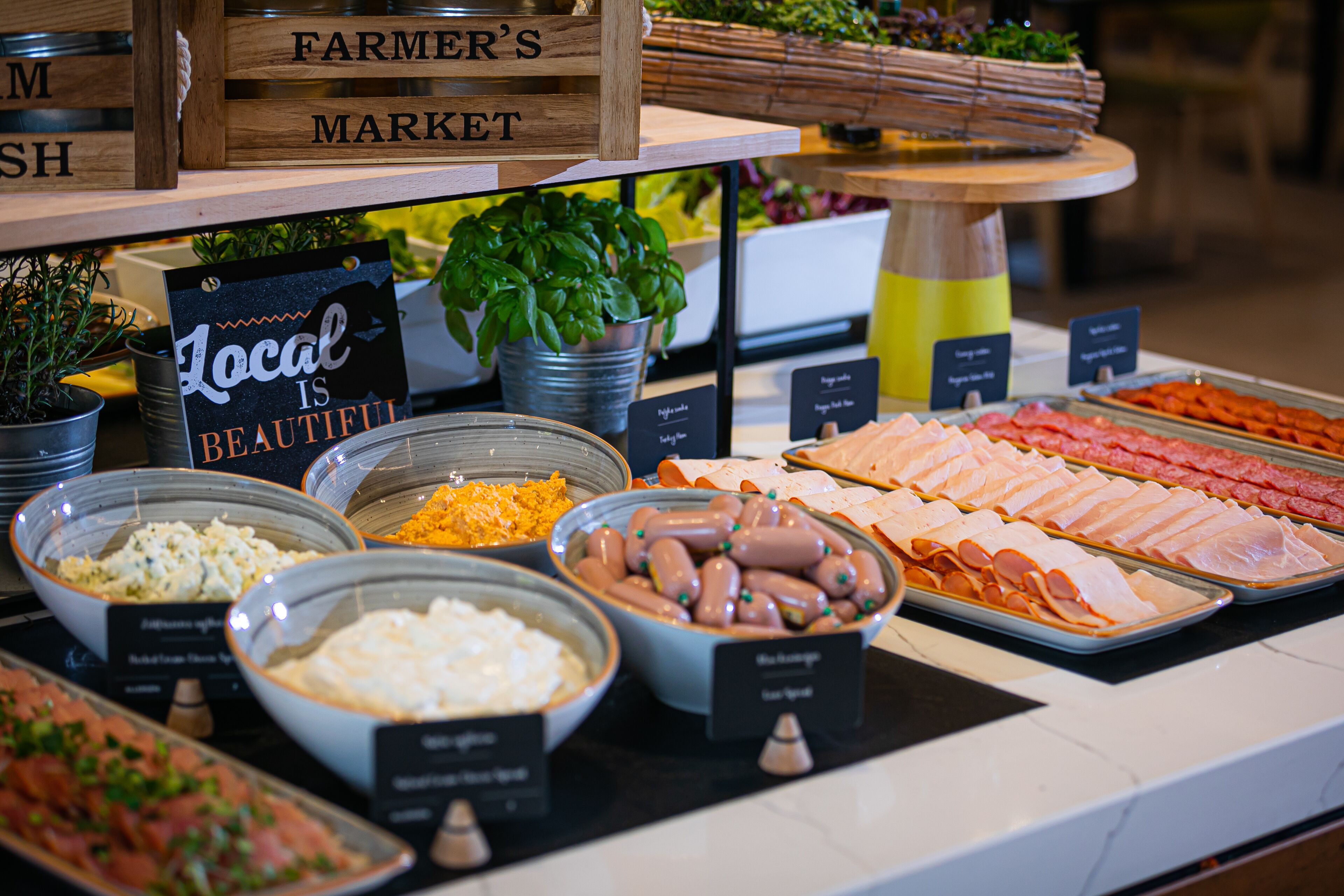 Un bufé con diversas opciones de comida, como carnes, quesos y ensaladas, exhibidas sobre un mostrador con etiquetas.