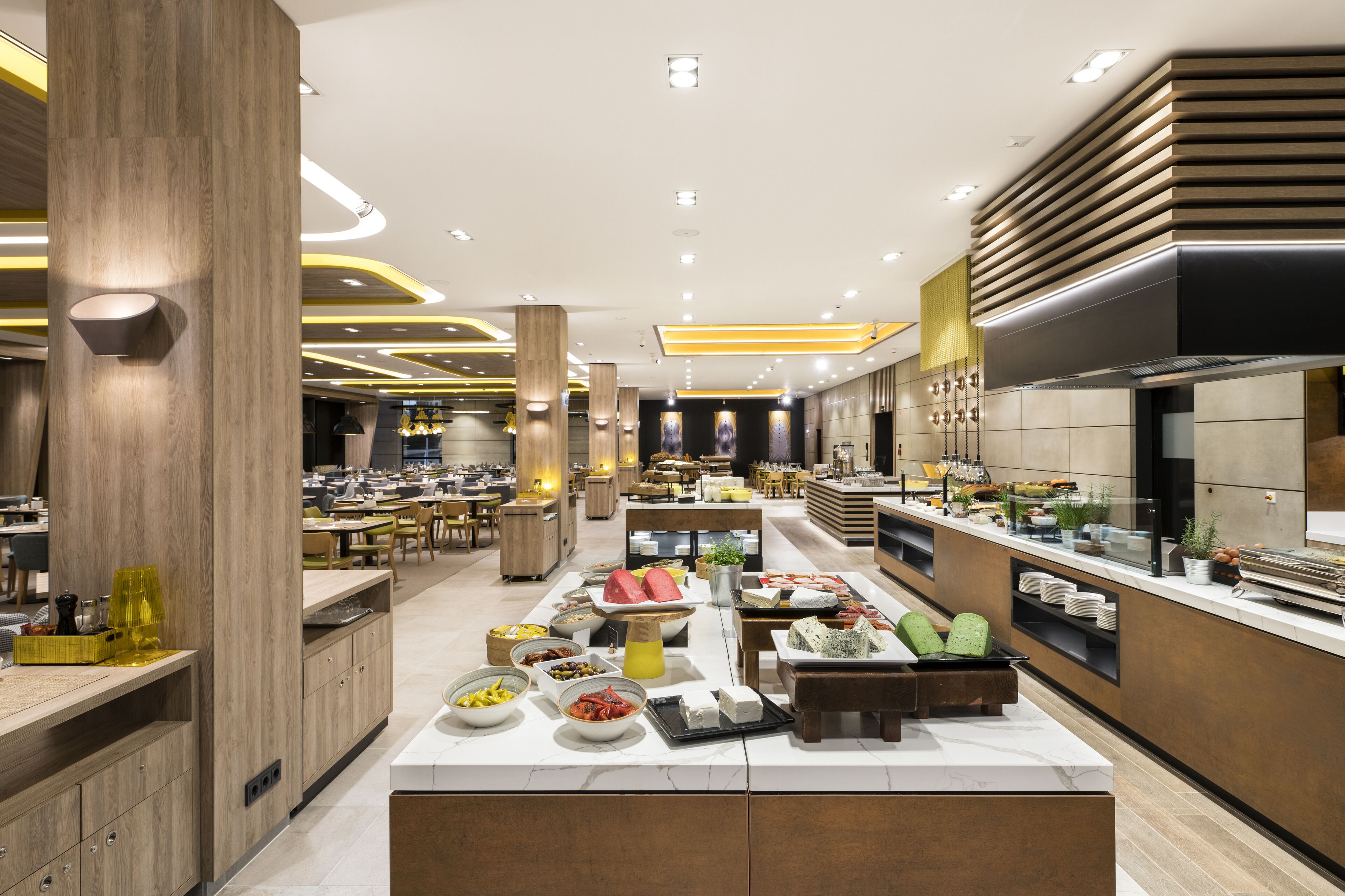 En moderne restaurant med et centralt buffetområde, trædetaljer og et lyst, veloplyst interiør.