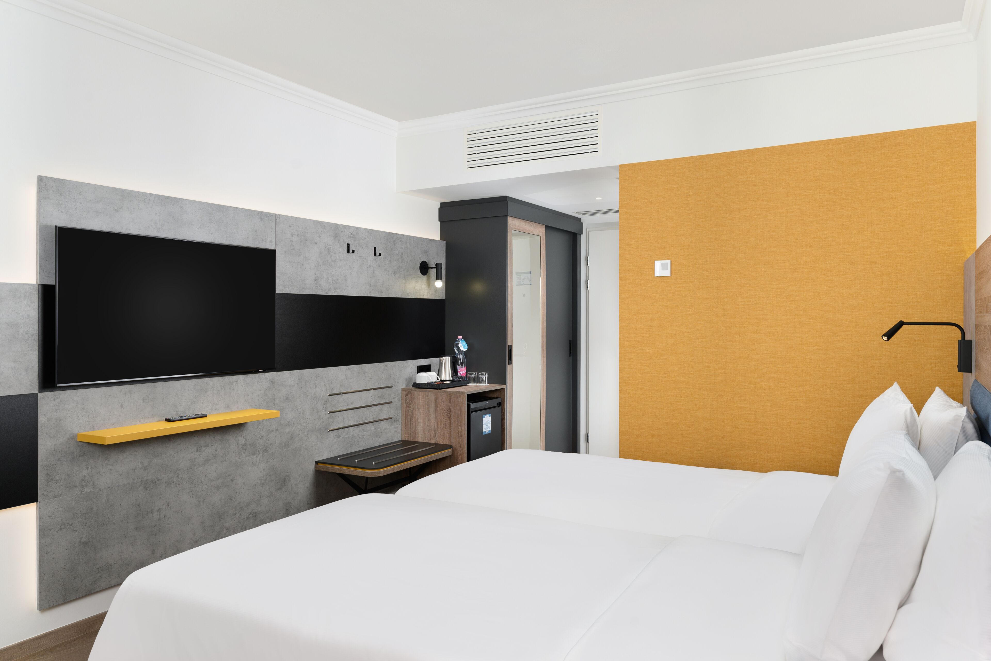 Une chambre d’hôtel moderne dotée d’un grand lit, d’une télévision à écran plat, d’un petit bureau et d’une armoire.