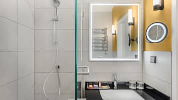 Un baño moderno con cabina de ducha de vidrio, un espejo grande y una encimera negra con lavamanos y artículos de aseo.