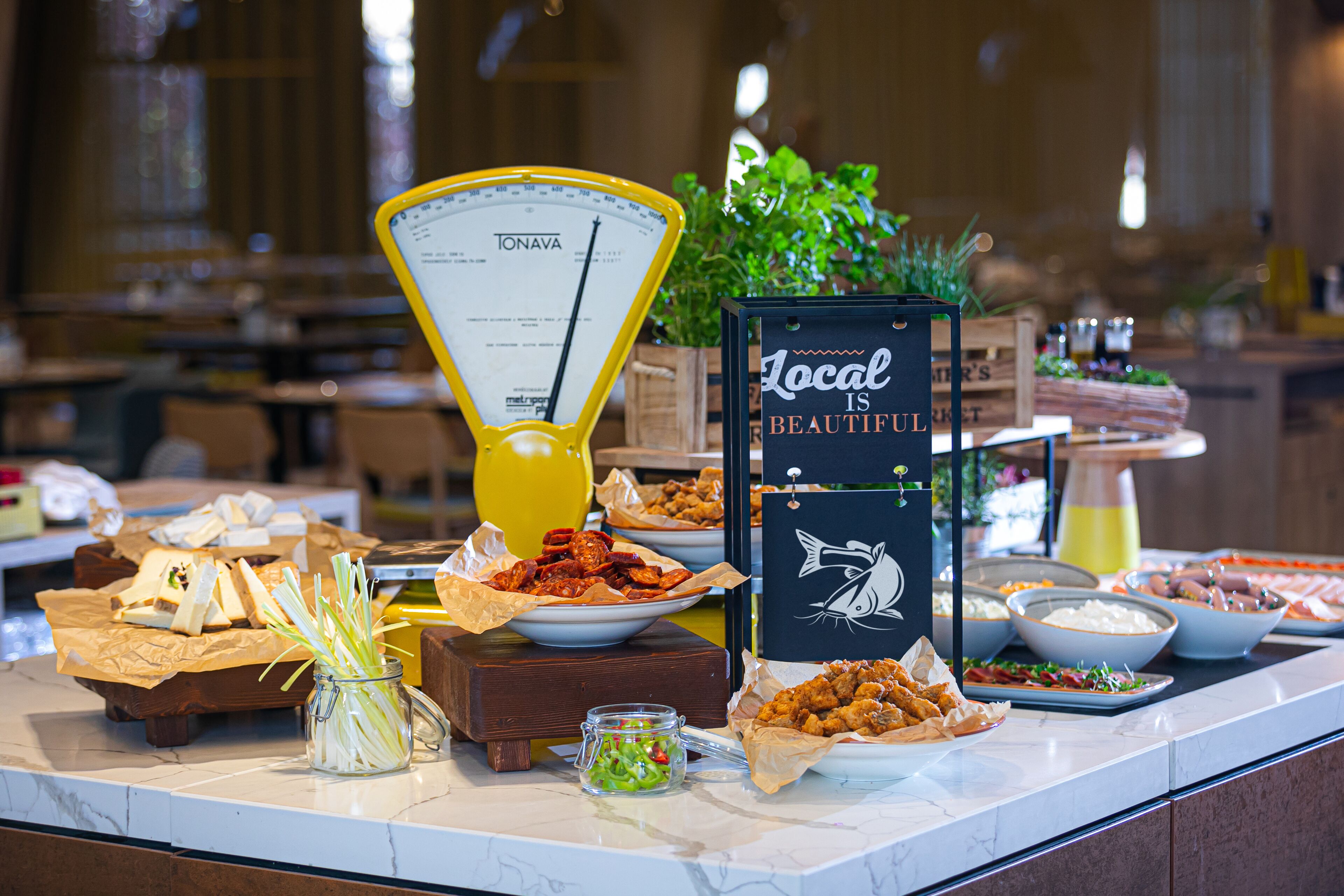Un buffet con diversi cibi, una bilancia e un cartello con la scritta 'Local is Beautiful'.