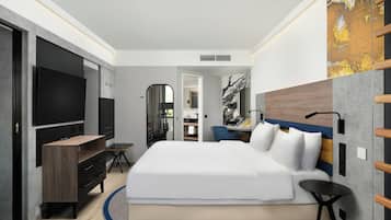 A modern hotel room with a large bed, a flat-screen TV, a desk, and a mirror.