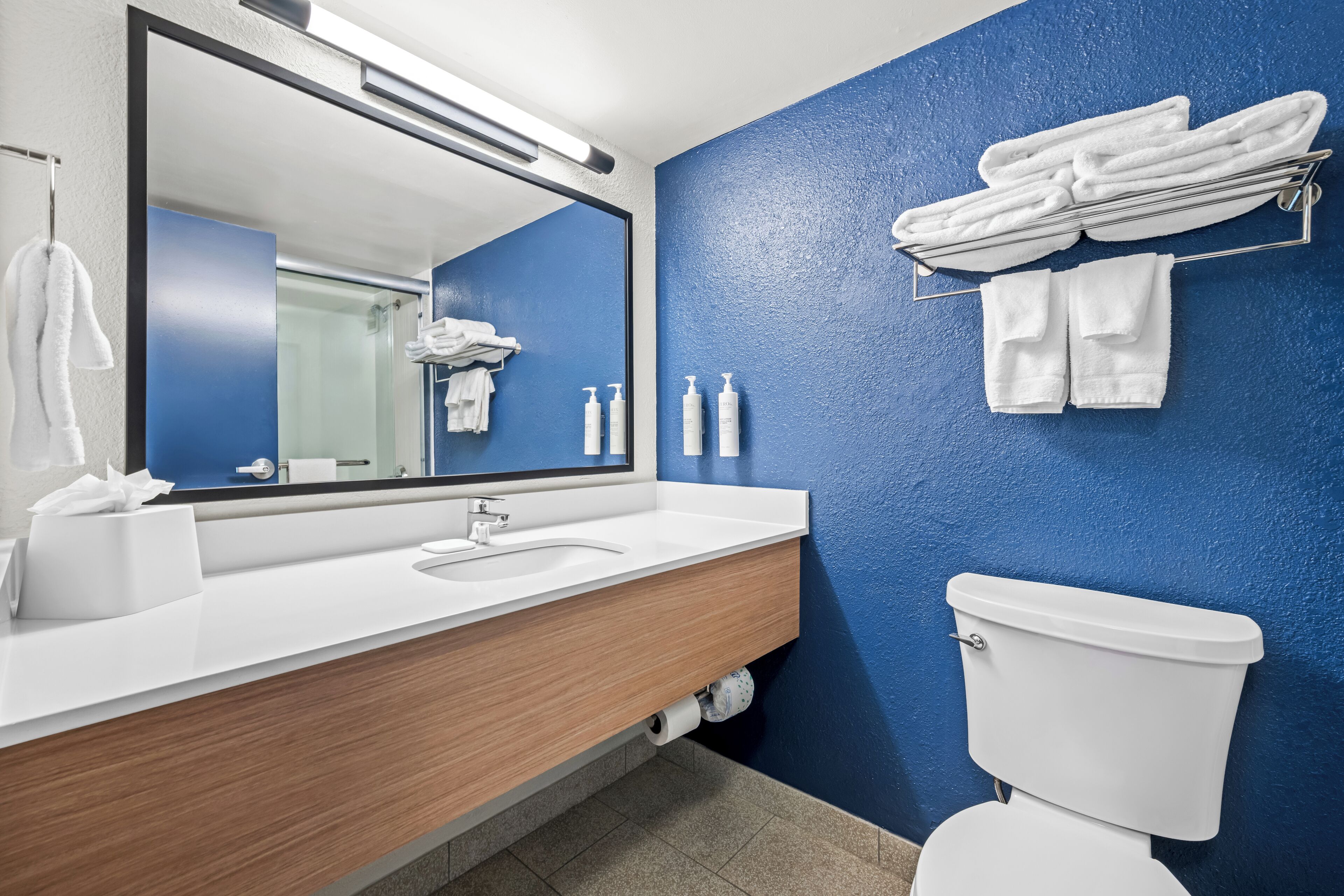 Une salle de bain moderne avec un mur d’accent bleu, un meuble-lavabo en bois, un lavabo blanc et des toilettes.