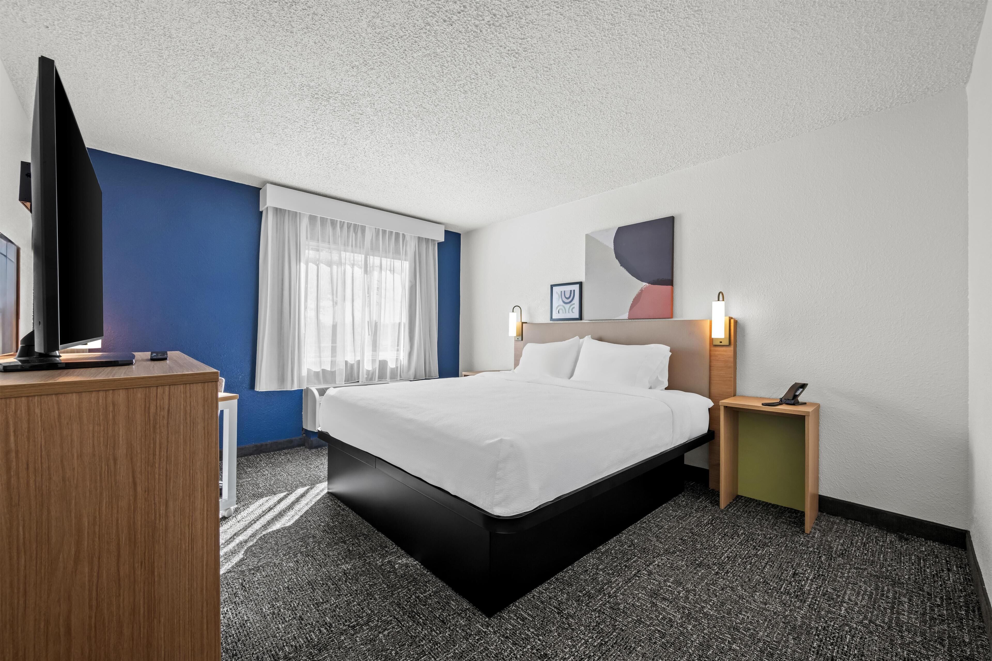 Une chambre d’hôtel avec un lit, un bureau, une télévision et une table de chevet avec une lampe.