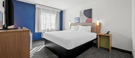 Une chambre d’hôtel avec un lit, un bureau, une télévision et une table de chevet avec une lampe.