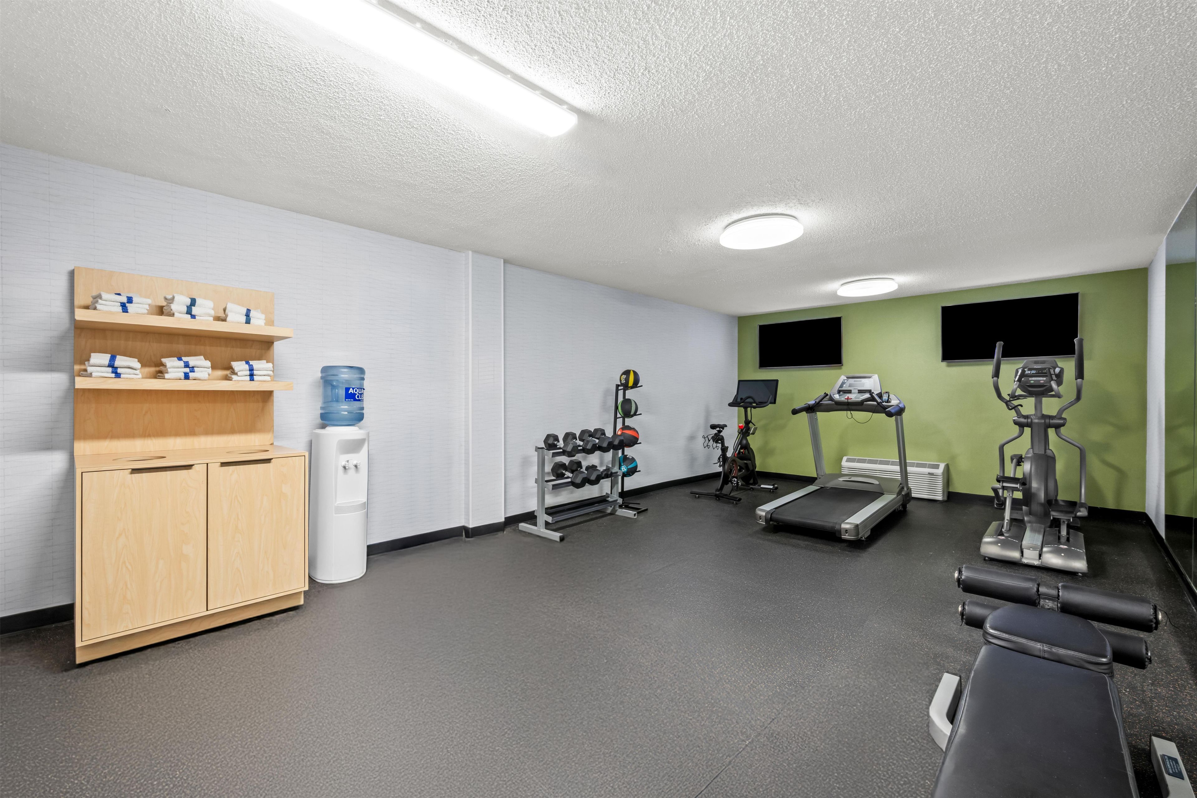 Un gimnasio con equipamiento de ejercicio, dispensador de agua y un perchero para toallas.