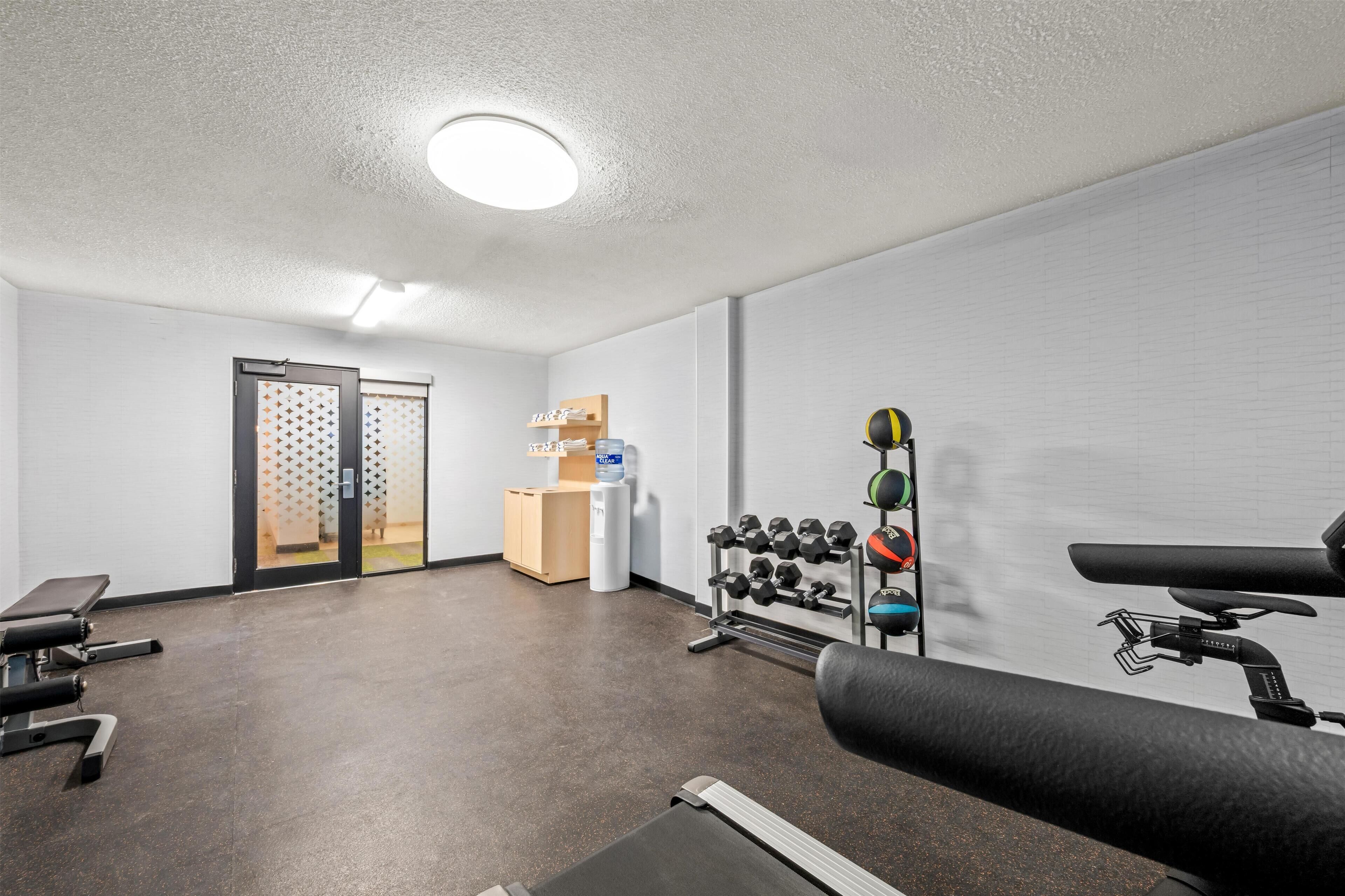 Ett gym med träningsutrustning, en vattenautomat och ett litet träskåp.