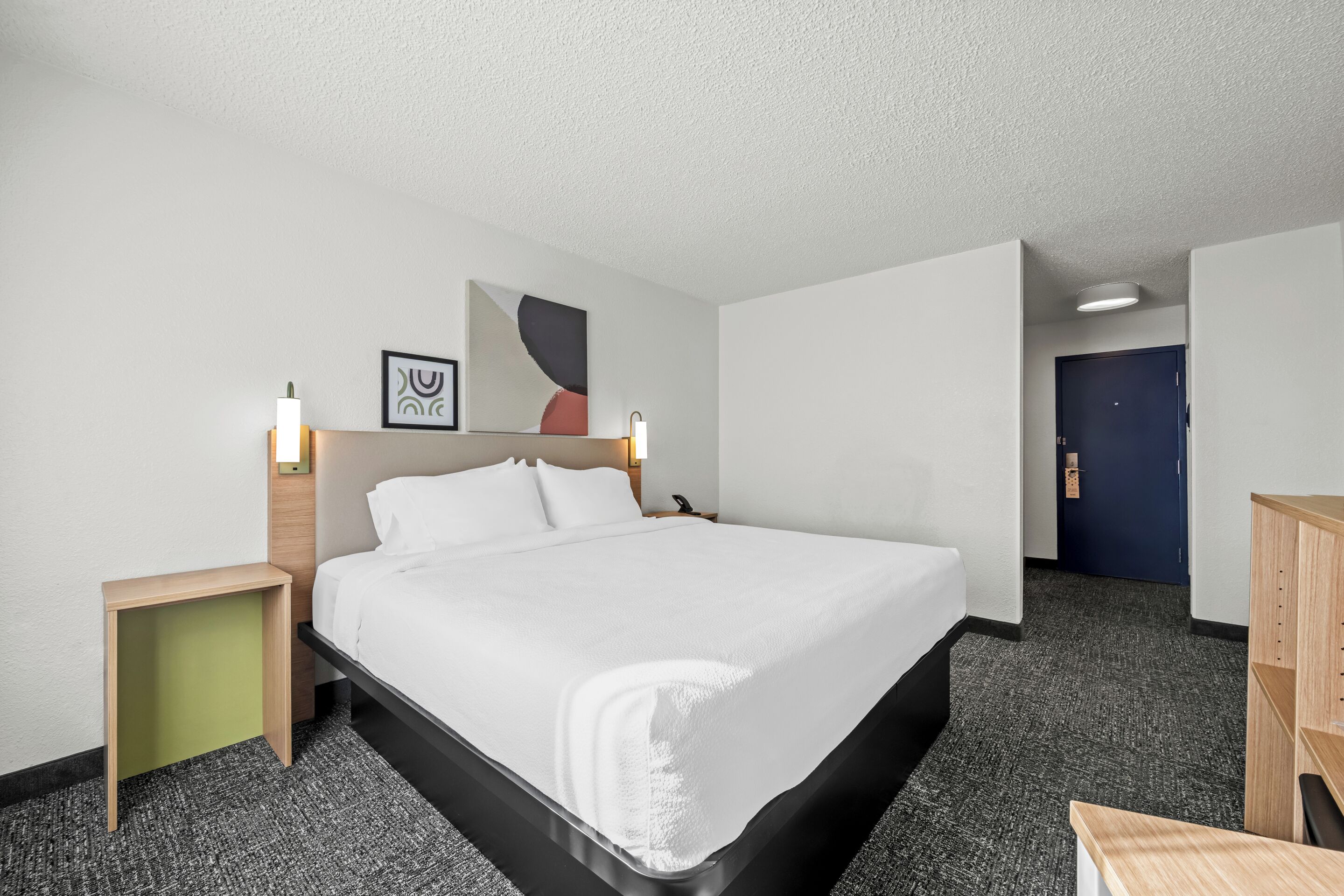 Una habitación de hotel con una cama grande, una mesita de noche, un escritorio y una puerta.