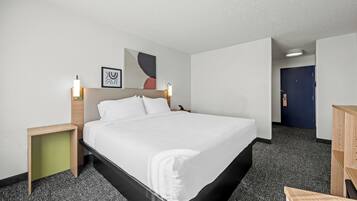 A hotel room with a large bed, a bedside table, a nightstand, a desk, and a door.