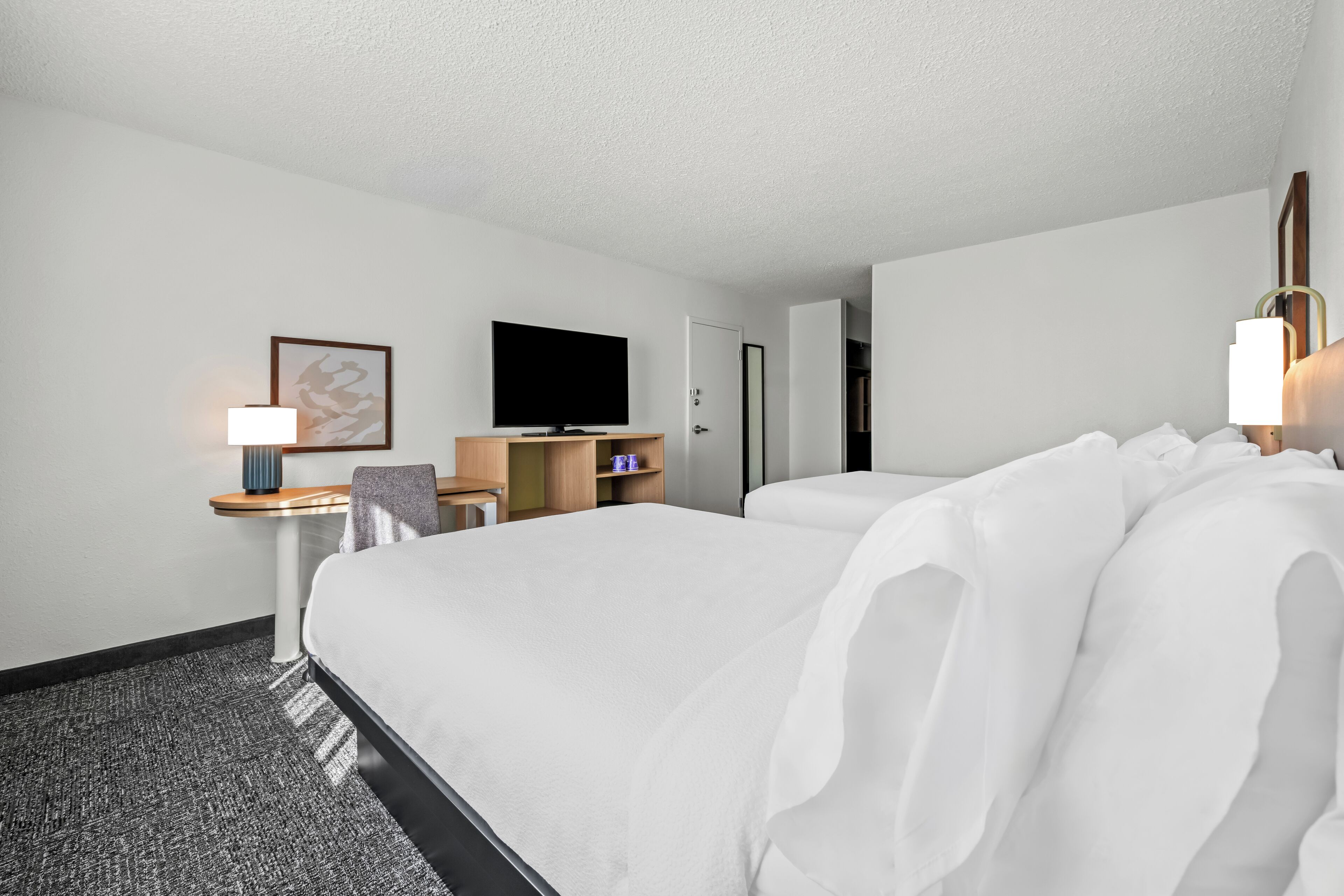 Una habitación de hotel con una cama grande, un escritorio con lámpara, televisión y armario.