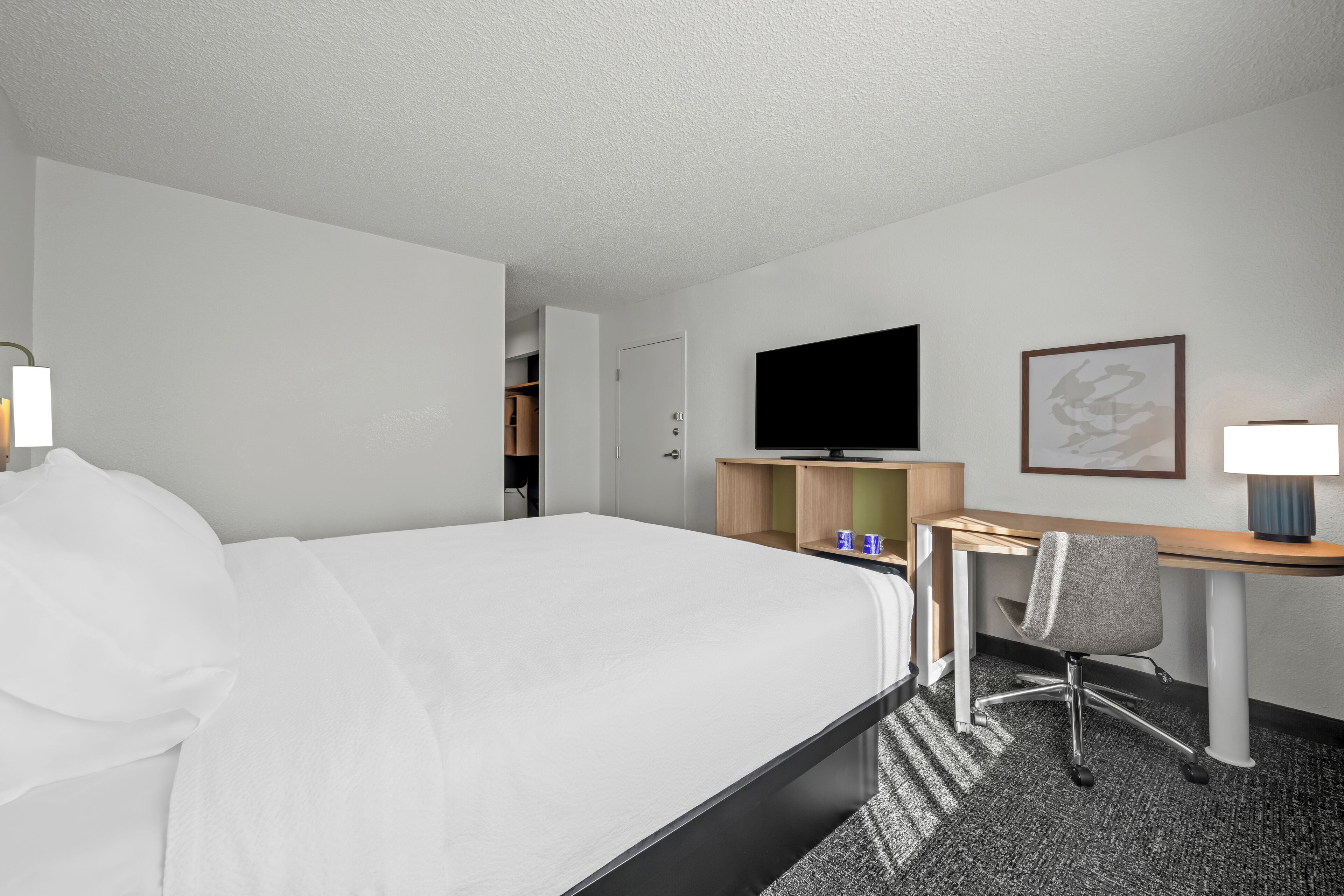 A hotel room with a large bed, a desk with a chair, a television, and a framed picture on the wall.