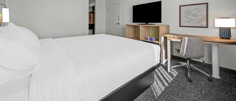Une chambre d’hôtel avec un grand lit, un bureau avec une chaise, une télévision et un tableau encadré au mur.
