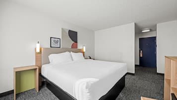 A hotel room with a large bed, bedside tables, a desk, and a door leading to another room.